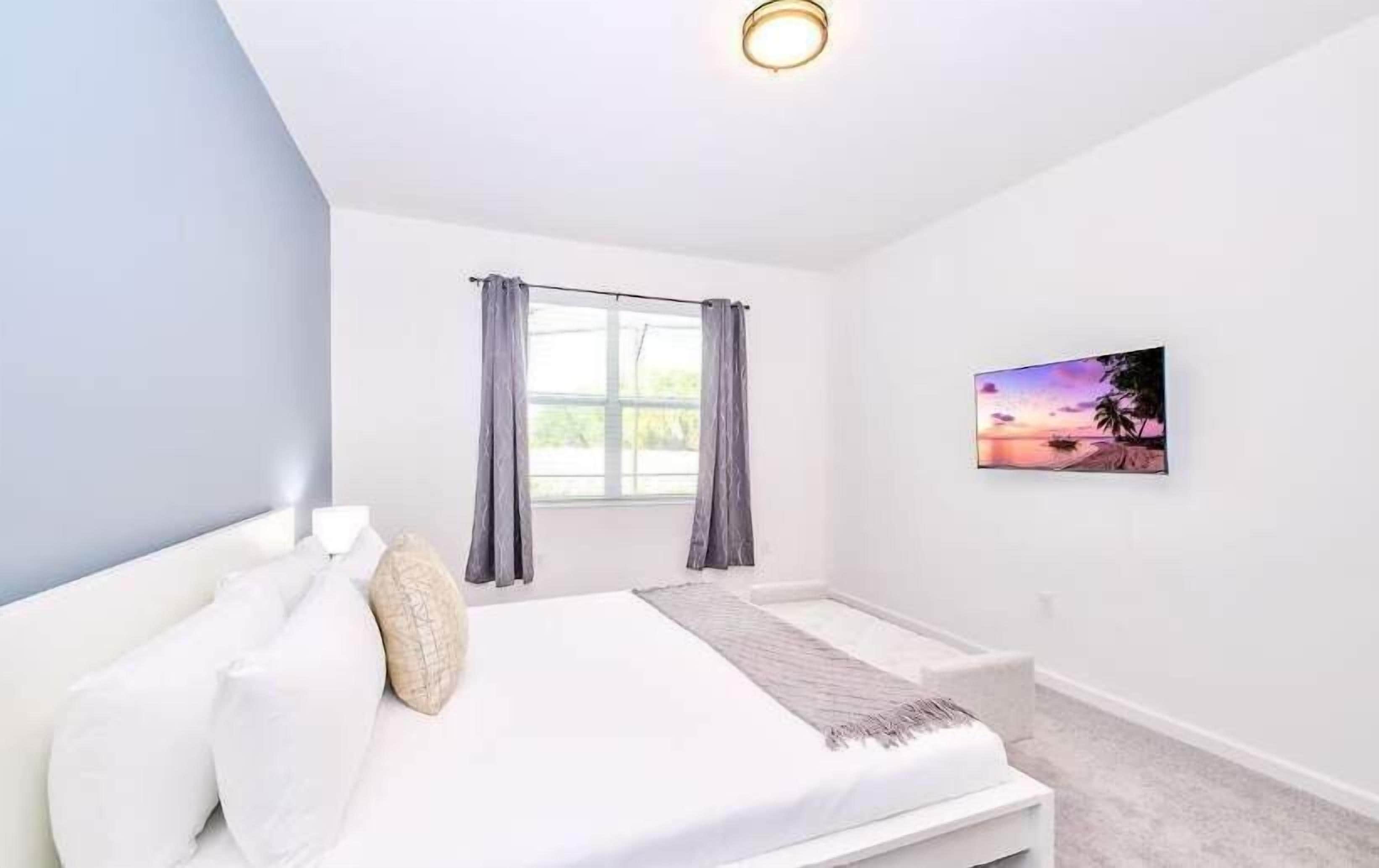 Une chambre à coucher avec un lit, une fenêtre avec des rideaux, un tableau au mur et un luminaire.