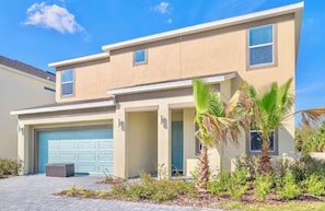 A two-story house with a garage, a covered patio, and a small garden with palm trees. - 8BR Near Disney | Private Pool & Hot Tub (Kissimmee)