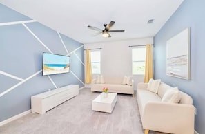 A modern living room with a flat-screen TV, a ceiling fan, and a large window with curtains. - 8BR Near Disney | Private Pool & Hot Tub (Kissimmee)