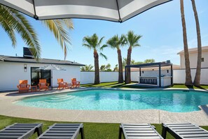 Ein Swimmingpool mit Liegestühlen und Grillplatz, umgeben von Palmen und einer weißen Mauer.