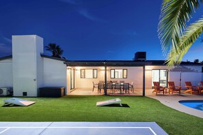 Ein modernes Haus mit einer überdachten Terrasse, einem Pool und einem gepflegten Rasen.