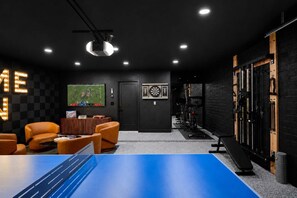 A room with a ping pong table, leather chairs, a dartboard, and exercise equipment. - Cactus Palms -Pool-Pickleball-Sports Court-Games (Scottsdale)
