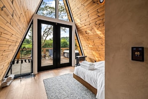 A triangular wooden room with a bed, a fire feature, and a thermostat. - Hodo Springs — Birch | A-Frame | Private Sauna, Hot Tub | River Access | Smokies (Sevierville)