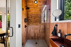 A modern bathroom with wooden paneling, a glass shower enclosure, and a sink with a mirror. - Hodo Springs — Cedar | Romantic A-Frame | Private Sauna, Hot Tub | Smokies (Sevierville)