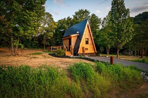 A wooden cabin with a sloped roof, surrounded by trees and a gravel path. - Hodo Springs — Cedar | Romantic A-Frame | Private Sauna, Hot Tub | Smokies (Sevierville)