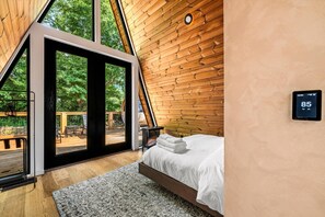 A bedroom with a bed, a thermostat, and a view of the outdoors. - Hodo Springs — Cedar | Romantic A-Frame | Private Sauna, Hot Tub | Smokies (Sevierville)