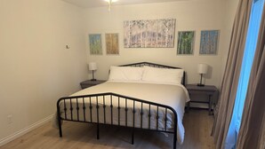 Ein Schlafzimmer mit einem Bett, zwei Nachttischen und einem Beistelltisch. Vier Bilder hängen an der Wand.