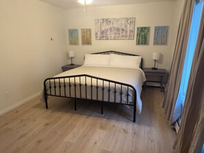 Ein Schlafzimmer mit einem Bett, zwei Nachttischen und einem Beistelltisch. Vier Bilder hängen an der Wand.