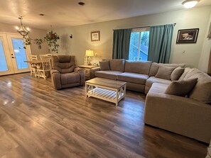 Ein Wohnzimmer mit Sofa, Sessel, Couchtisch, Esstisch, Stühlen und einer Chandelier.