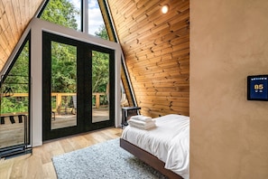 A bedroom with a bed, a digital thermostat, and a view of the outdoors. - Hodo Springs — Maple | Luxury A-Frame | Private Sauna, Hot Tub | River | Smokies (Sevierville)