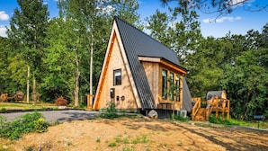 A modern, triangular wooden cabin with a sloped roof, surrounded by dense forest. - Hodo Springs — Maple | Luxury A-Frame | Private Sauna, Hot Tub | River | Smokies (Sevierville)