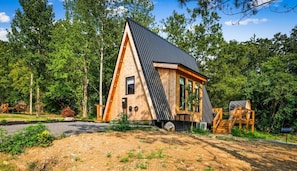 A modern, triangular wooden cabin with a sloped roof, surrounded by dense forest. - Hodo Springs — Maple | Luxury A-Frame | Private Sauna, Hot Tub | River | Smokies (Sevierville)