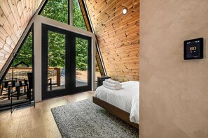 A bedroom with a wooden sloped ceiling, a bed with white bedding, and a thermostat on the wall. - Hodo Springs — Pine | A-Frame | Forest Sauna Path + Hot Tub | Smokies (Sevierville)