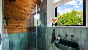 Une salle de bain moderne avec un plafond en bois, une grande fenêtre donnant sur les arbres, un miroir rond et un lavabo vert.