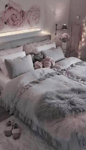 Una camera da letto con un letto, cuscini, un tappeto morbido e ciabatte.