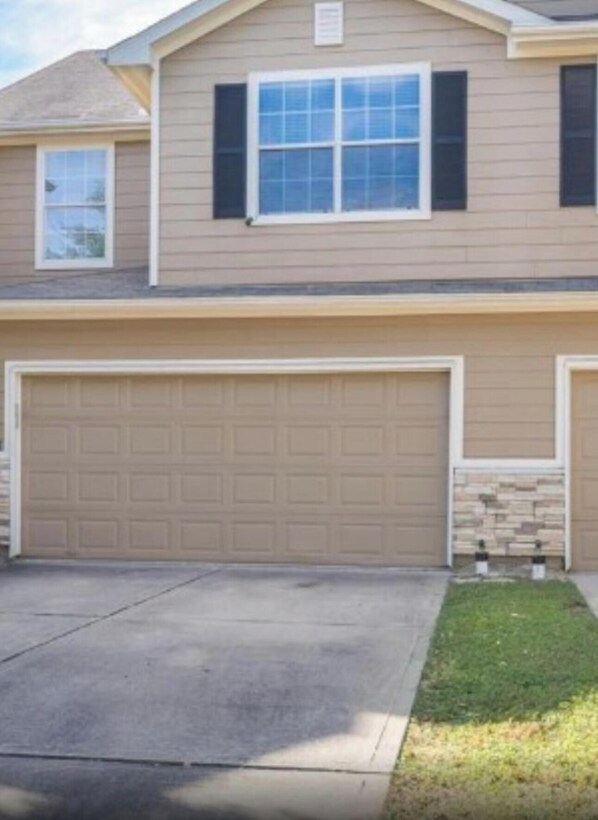 Una casa a due piani con un garage, un piccolo giardino antistante e un muro a secco decorativo.