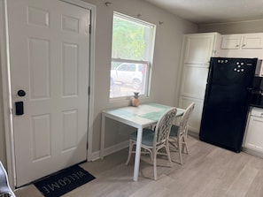 Une petite cuisine avec un réfrigérateur noir, une fenêtre donnant sur une voiture garée et une table avec des chaises.
