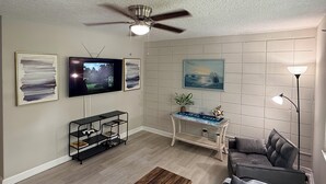 Ein Wohnzimmer mit Deckenventilator, Fernseher, Wandkunst, einem Konsolentisch und einer Couch.
