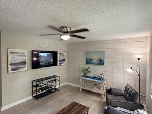 Un salon avec un ventilateur de plafond, un téléviseur, des œuvres d’art accrochées au mur, une console et un canapé.