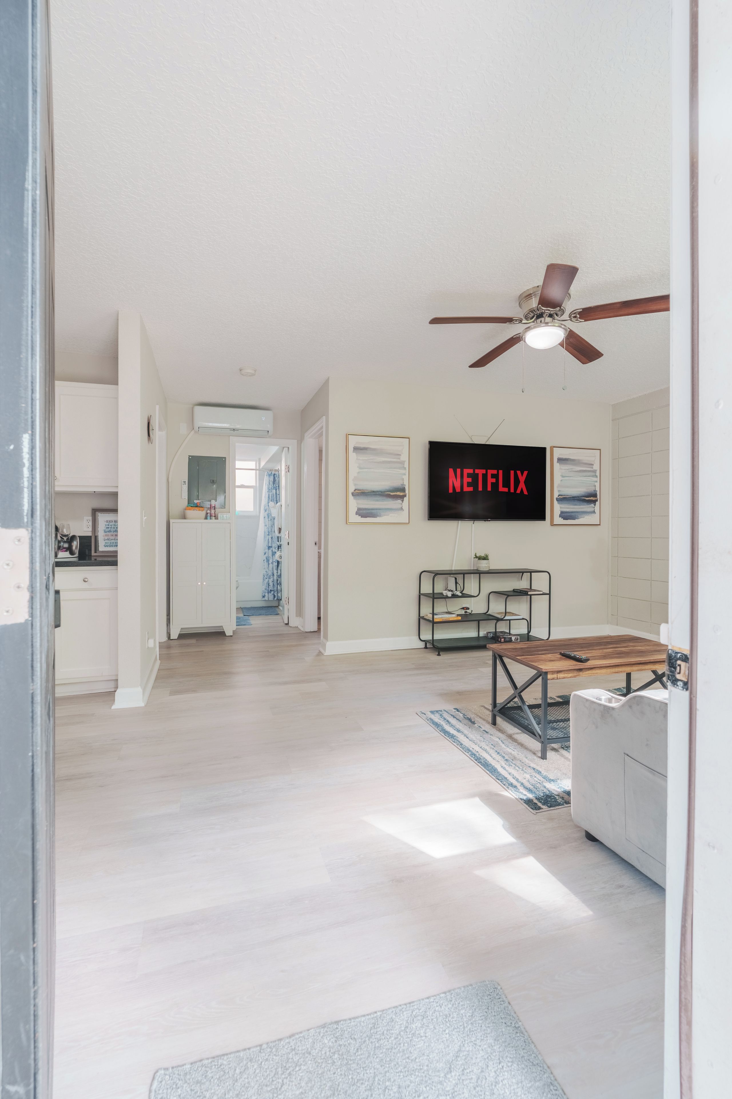A spacious living room with a ceiling fan, a flat-screen TV displaying 'NETFLIX', and a wooden coffee table.