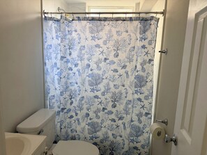 Une salle de bain équipée de toilettes, d’un lavabo et d’un rideau de douche orné d’un motif représentant la vie marine.