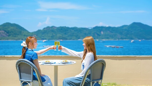 Two people toasting at a table with a view of the sea and mountains in the background. - Hotel O. Naruto (Naruto)