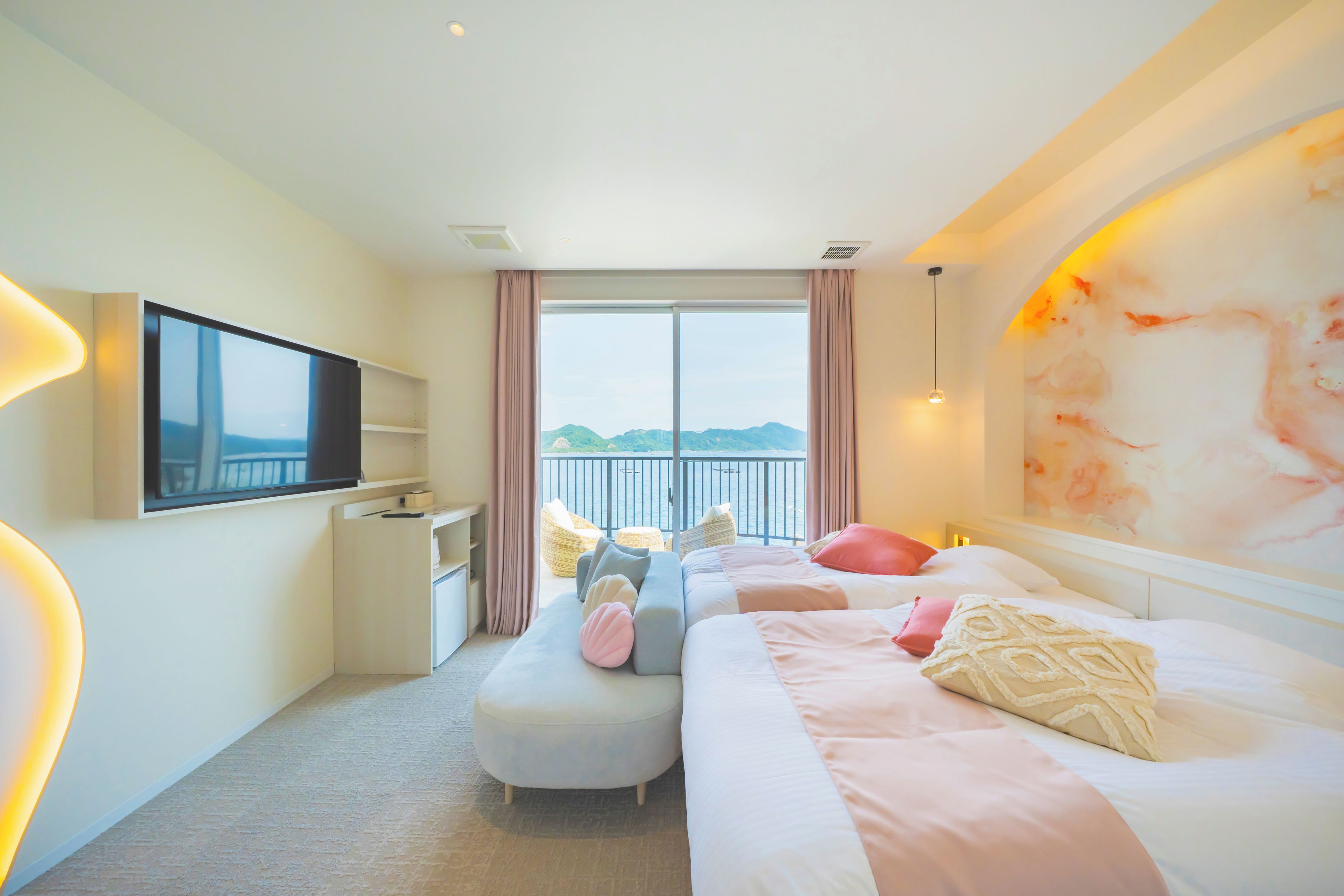 A hotel room with a bed, a TV, a desk, a chair, and a view of the sea.