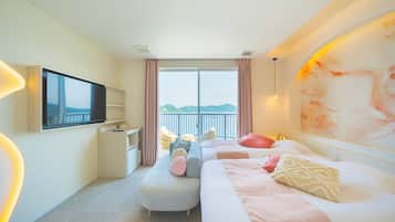 A hotel room with a bed, a TV, a desk, a chair, and a view of the sea.