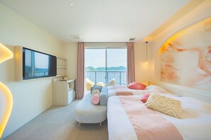 A hotel room with a bed, a TV, a desk, a chair, and a view of the sea.