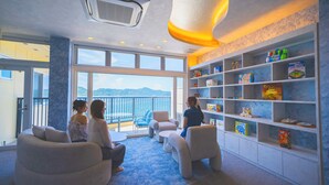 A room with a large window overlooking the sea, a children's play area with toys, and a seating area with sofas and chairs. - Hotel O. Naruto (Naruto)