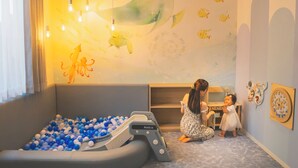 A playroom with a ball pit, a child playing with a toy kitchen set, and a wall with fish and octopus decals.