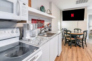 Une cuisine moderne équipée d’un four encastré, d’un micro-ondes et d’une machine à café. Un coin repas est aménagé avec une table et des chaises en bois.