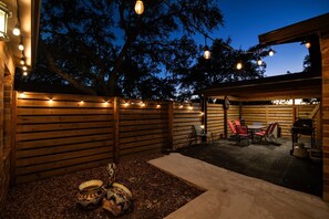 An outdoor patio area with wooden walls, string lights, a table with chairs, and decorative bowls. - Canyon Lake · 4BR Home + Suite · Sleeps 10 · Pets OK (Canyon Lake)
