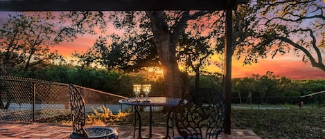 An outdoor patio with a pergola, two metal chairs, a table, and a view of a sunset.