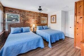 Une pièce avec deux lits, un mur en briques, un ventilateur de plafond et une porte.