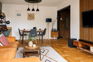 A modern living room with a sofa, dining table, chairs, a coffee table, a TV, and a bookshelf. - Appartement Sérénité Charonne - Welkeys (Paris)