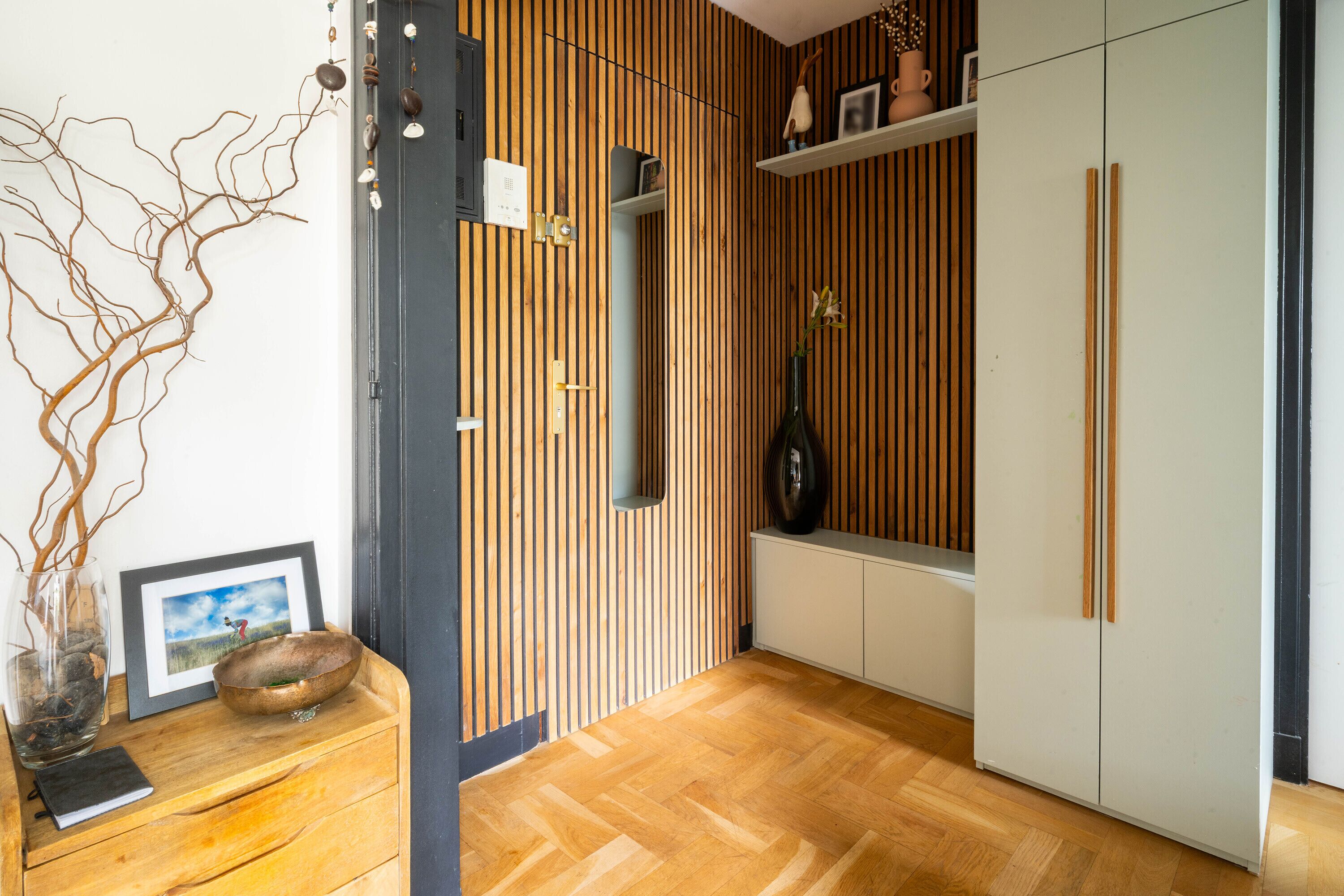 A modern interior with a wooden floor, a white cabinet, and a wall-mounted shelf with decorative items.