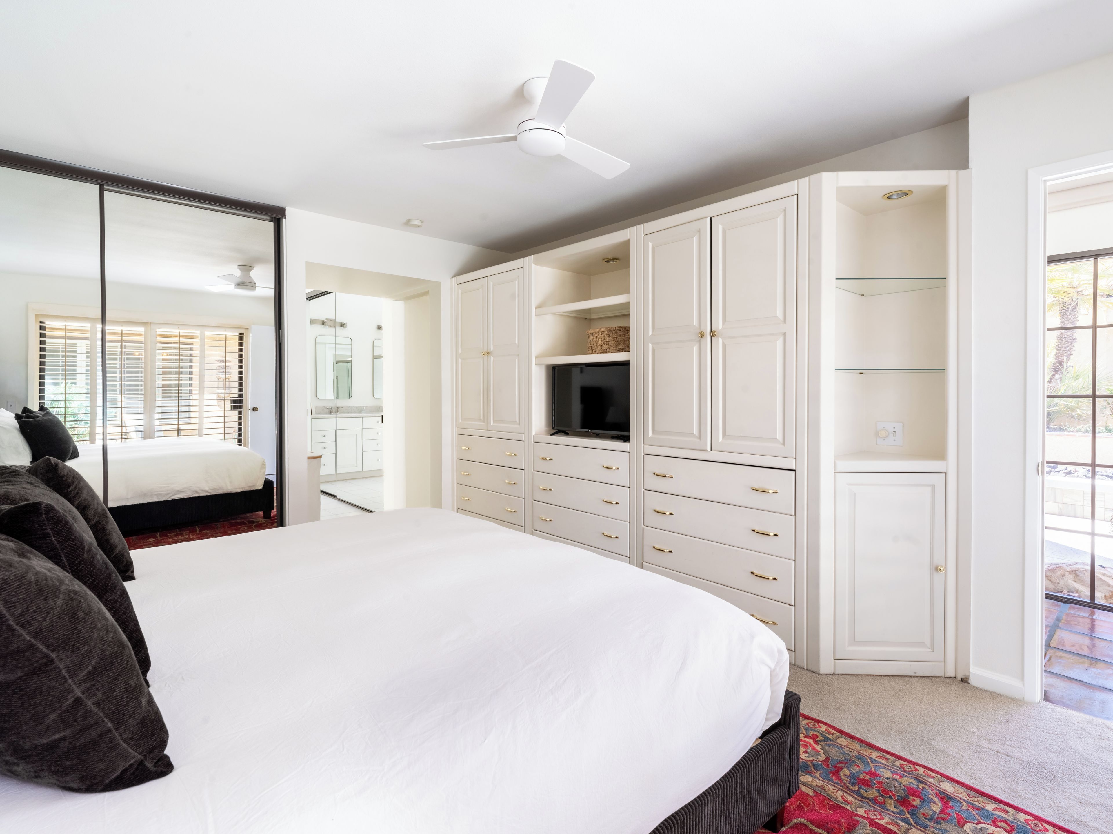 A bedroom with a bed, a wardrobe, a television, and a ceiling fan.