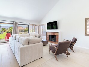 Ein modernes Wohnzimmer mit einer Couch, Sesseln, einem Kamin und einem an der Wand befestigten Fernseher.