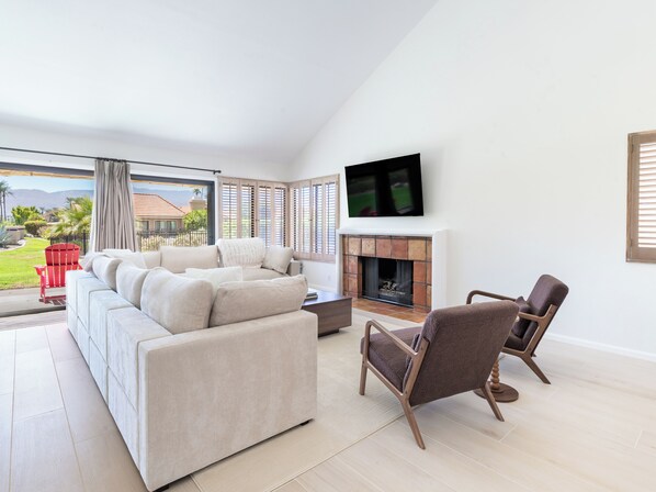 Ein modernes Wohnzimmer mit einer Couch, Sesseln, einem Kamin und einem an der Wand befestigten Fernseher.