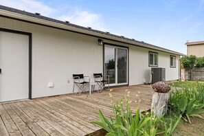 A modern house with a wooden deck, a sliding glass door, and a small outdoor seating area with chairs.