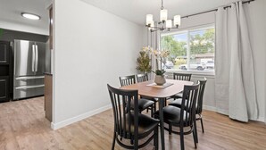 Eine moderne Küche mit Edelstahlgeräten, ein Essbereich mit Holztisch und schwarzen Stühlen sowie ein Fenster mit Vorhängen.