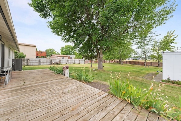 A backyard with a wooden deck, a large tree, and a grassy lawn.