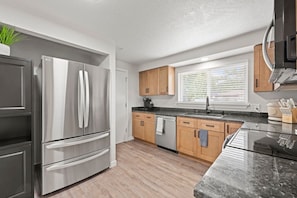 A modern kitchen with stainless steel appliances, wooden cabinets, and a granite countertop.
