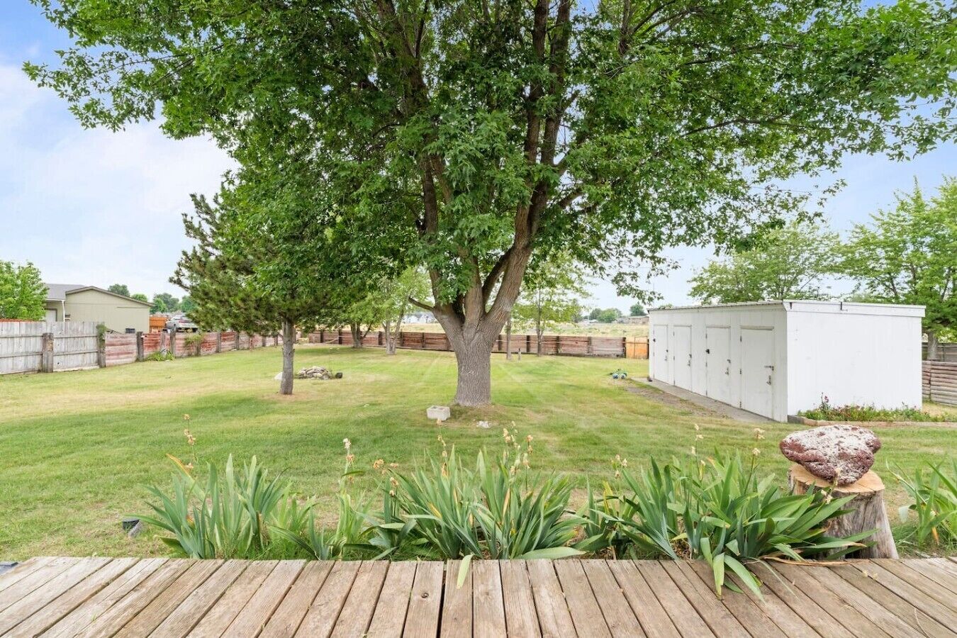 Un patio trasero con un árbol grande, una terraza de madera y un cobertizo.