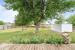 Un patio trasero con un árbol grande, una terraza de madera y un cobertizo.