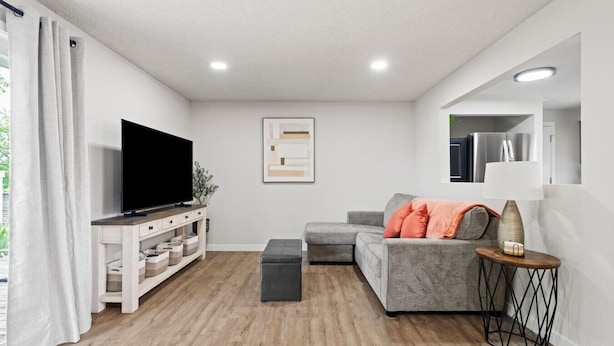 Ein modernes Wohnzimmer mit Fernseher, grauem Sofa, Holzboden und einem Beistelltisch mit Lampe.