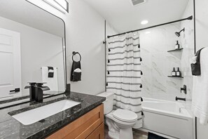 A modern bathroom with a large mirror, a sink, a toilet, and a shower area.