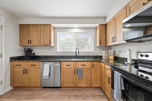 Una cocina moderna con armarios de madera, lavavajillas de acero inoxidable, encimera negra y horno empotrado.