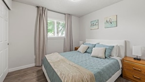 Ein Schlafzimmer mit Bett, Nachttischen, einem Fenster mit Vorhängen und Wandbildern.